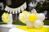 Yellow and white balloon flower arrangement on display with matching yellow and white decorations blurred in background