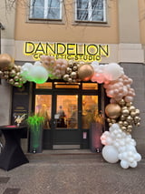 Dandelion Esthetic Studio storefront with yellow neon sign and colorful balloon clusters in gold, pink, and white decorating the entrance