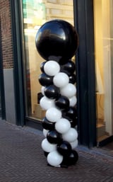 Black and white balloon tower sculpture with large sphere on top displayed outside a storefront